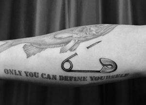 Фото тату: реалистичный рисунок булавки с надписью "ONLY YOU CAN DEFINE YOURSELF" на руке. Черно-белая татуировка с акцентом на самоопределение.
