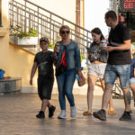 Фотография семьи, гуляющей по улице, с акцентом на уличную татуировку на руке мужчины. Снимок сделан в солнечный день.