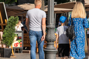 Фотография мужчины с татуировкой на руке, стоящего на улице. Видна татуировка в стиле геометрик и другие люди на заднем плане.
