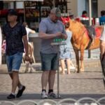 Фотография мастера тату, работающего на улице. Видна его татуировка на руке и оборудование для нанесения татуировок.