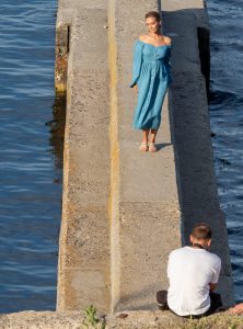 Фотография женщины в платье, стоящей у воды. На руке мужчины видна татуировка, частично скрытая одеждой.