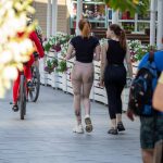 Фото двух девушек, идущих по улице в леггинсах с татуировками, и велосипедиста. Видны татуировки цветов, бабочек и надписи на ногах.