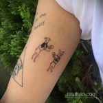 Фото минималистичной татуировки с изображением двух боксеров и надписью "with the family" на руке. Черно-белый рисунок татуировки с простыми линиями.