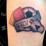 Фото тату футбольного мяча с римскими цифрами 'V-XCV' на ленте. Цветная татуировка, символизирующая дату или важную цифру.