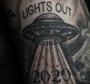 Черно-серое фото татуировки НЛО с надписью 'Lights Out' и годом '2020' на предплечье, выполненное в реалистичном стиле.