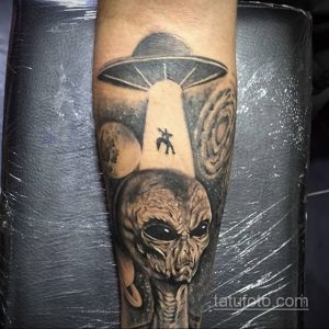 Фото реалистичного тату НЛО и головы инопланетянина. Черно-серый рисунок татуировки с высокой детализацией и использованием светотени.