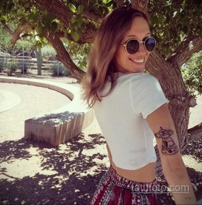 Фото тату на руке девушки: небольшая татуировка с изображением летающей тарелки над горами. Рисунок выполнен в простом, минималистичном стиле.