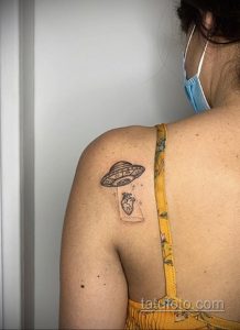 Фото нежной татуировки на спине: НЛО парит над банкой с сердцем, выполненной в минималистичном стиле с использованием тонких линий.
