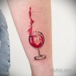 Фото тату на предплечье: акварельный рисунок бокала с красным вином, из которого стекают капли. Нежный и элегантный рисунок татуировки.