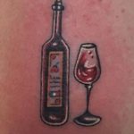 Фото тату: небольшая татуировка на коже с изображением бутылки красного вина и бокала. Минималистичный рисунок с использованием красных и черных оттенков.