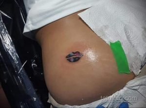 Фото тату акварельных губ на боку. Нежный рисунок татуировки выполнен в пастельных тонах с использованием техник акварели и брызг.