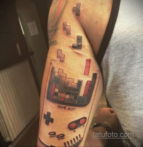Фото тату Game Boy на руке. Черно-белый рисунок с элементами пиксель-арта и детальной проработкой. Идеально для поклонников ретро-игр.