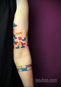 Фото тату, изображающее фигуры из игры Тетрис, расположенные на предплечье в ярких цветах: синем, красном, желтом и оранжевом.