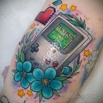 Фото тату с изображением портативной консоли Game Boy, играющей в Тетрис, украшенной цветами и звездами на руке.