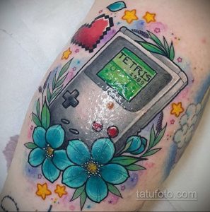Фото тату с изображением портативной консоли Game Boy, играющей в Тетрис, украшенной цветами и звездами на руке.