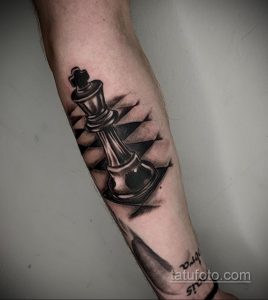 Фото тату на предплечье с изображением шахматного короля в стиле blackwork. Черно-белый рисунок с использованием плотных черных заливок и геометрических элементов.