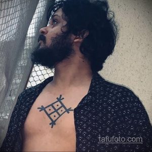 Фото тату: изображение славянского символа Чернобога, выполненное в графическом стиле на груди мужчины.