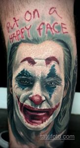 Цветная татуировка Джокера с надписью "Put on a happy face", выполненная на руке.