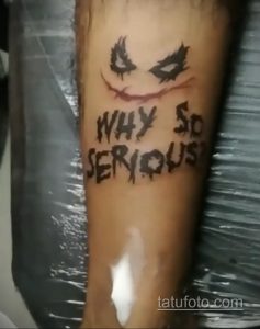 Фото тату на руке с надписью "WHY SO SERIOUS?" и изображением улыбки Джокера. Минималистичный дизайн и черно-белое исполнение.
