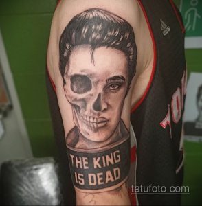 Фото тату Элвиса Пресли в виде скелета с надписью "The King is Dead", выполненное в черно-серых тонах. Реалистичный череп и надпись.