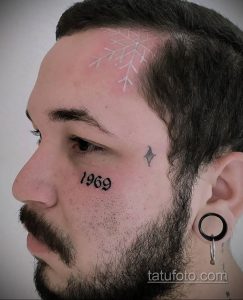 Фото татуировки снежинки на виске мужчины, рядом с датой '1969' и небольшим символом. Рисунок выполнен в минималистичном стиле.