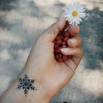 Фото тату маленькой снежинки на запястье. Черно-белый рисунок татуировки, выполненный тонкими линиями, выглядит изящно и минималистично.