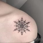 Фотография татуировки снежинки на плече, выполненной в технике дотворк. Детализированный рисунок татуировки с использованием множества точек для создания объема и текстуры.