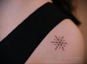 Фото минималистичной татуировки на плече с изображением простой снежинки, выполненной тонкими черными линиями.