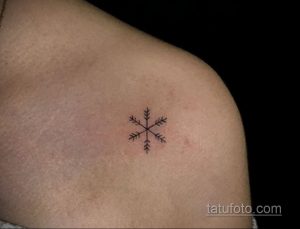 Фото минималистичной татуировки снежинки на плече. Черно-белый рисунок с четкими линиями и небольшим количеством деталей.