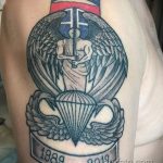 Фото тату на плече с изображением символа воздушно-десантных войск: парашют, крылья и надпись Airborne. Черно-белый рисунок татуировки.