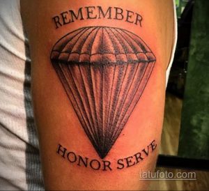 Фото тату на руке: стилизованный парашют с надписями 'REMEMBER' и 'HONOR SERVE'. Простой, но выразительный рисунок татуировки в черно-серых тонах.