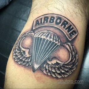 Фото тату на предплечье: парашют с крыльями и надписью 'AIRBORNE'. Черно-серый рисунок татуировки, символизирующий принадлежность к воздушно-десантным войскам.