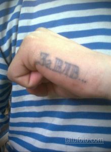 Фото тату на руке: надпись 'За ВДВ' выполненная простым шрифтом на фоне полосатой ткани.