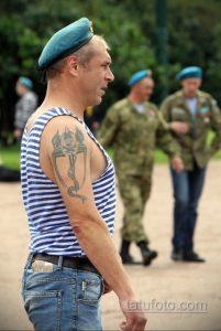 Фото татуировки на плече с изображением черепа в берете, под которым раскрывается парашют. Черно-серый рисунок.