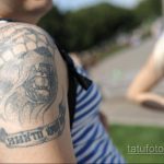 Фото татуировки на плече с изображением черепа в кокарде. Тату выполнено в черно-серых тонах, выглядит выцветшим и потертым.
