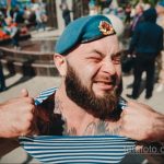 Фото мужчины с бородой в берете и татуировками на руках и шее, выполненными в различных стилях.
