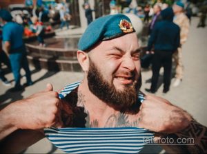 Фото мужчины с бородой в берете и татуировками на руках и шее, выполненными в различных стилях.