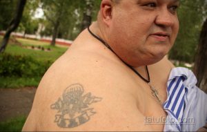 Фото татуировки на плече: изображение раскрытого парашюта с надписью, выполненное в черно-серых тонах.
