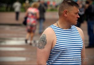 Фото старой татуировки на плече мужчины: изображение орла с раскрытыми крыльями и парашютом, выполненное в синих и черных тонах.