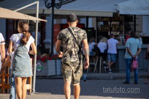 Фотография мужчины, идущего спиной вперед, с видимыми татуировками на спине, плечах и руках.
