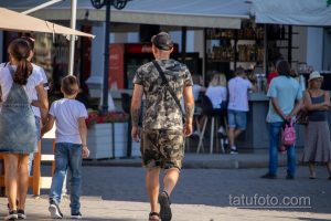Фотография мужчины, идущего спиной вперед, с видимыми татуировками на спине, плечах и руках.