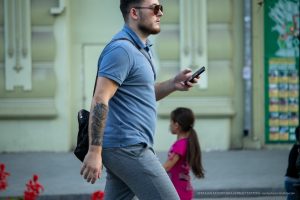 Фото мужчины с татуировкой на руке, идущего по улице. Видна татуировка, покрывающая большую часть предплечья. Уличная татуировка.