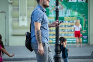 Фото мужчины с татуировкой на руке, идущего по улице. Видна татуировка, покрывающая большую часть предплечья. Уличная татуировка.