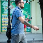 Фото мужчины с татуировкой на руке, разговаривающего по телефону. Видна татуировка, покрывающая большую часть предплечья. Уличная татуировка.