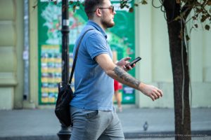 Фото мужчины с татуировкой на руке, разговаривающего по телефону. Видна татуировка, покрывающая большую часть предплечья. Уличная татуировка.
