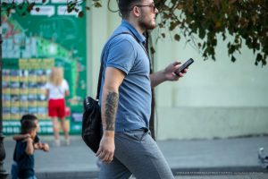 Фото мужчины с татуировкой на руке, идущего по улице. Видна татуировка, покрывающая большую часть предплечья. Уличная татуировка.