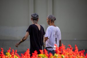 Фотография двух мужчин с татуировками на шее и руках, идущих по улице. Мужчины одеты в повседневную одежду и кепки.