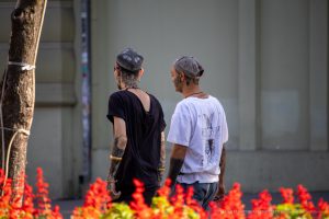 Фотография двух мужчин с татуировками на шее и руках, идущих по улице. Мужчины одеты в повседневную одежду и кепки.