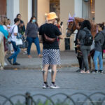Фотография мужчины в шляпе и с татуировкой на руке, стоящего на улице рядом с лошадью.