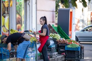 Фотография продавца на рынке с татуировкой на руке, обслуживающего покупателя. Виден фрагмент черно-серого рисунка татуировки на предплечье.